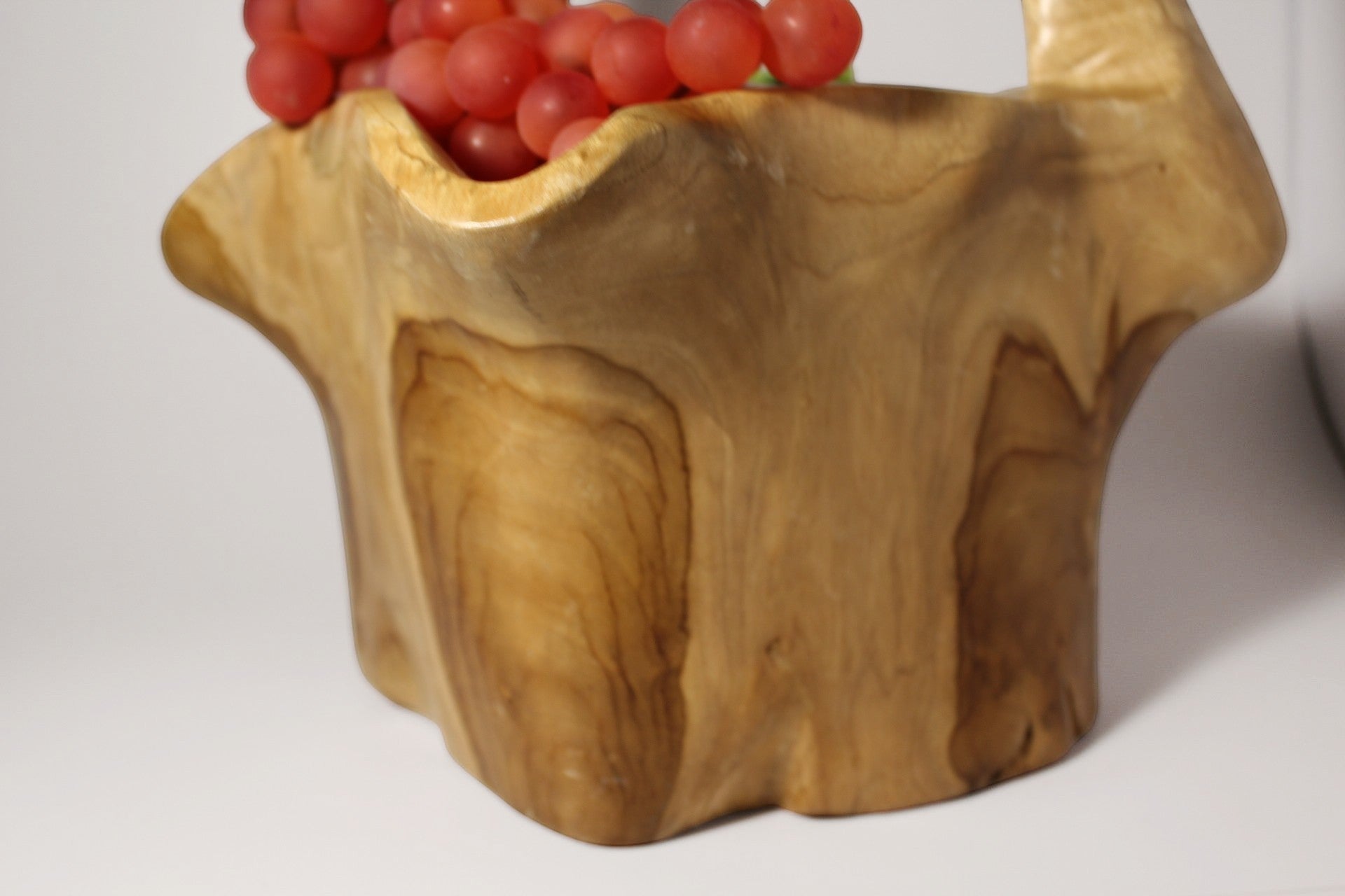 Natural Wonders USA burl wood basket with integrated handle, showcasing unique grain patterns and organic shape. Filled with red grapes.