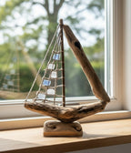 Natural Wonders USA sea glass and driftwood boat sculpture with white and blue glass sails on a wooden base.