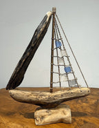 Natural Wonders USA sea glass and driftwood boat sculpture with blue and clear glass sails on a wooden base.