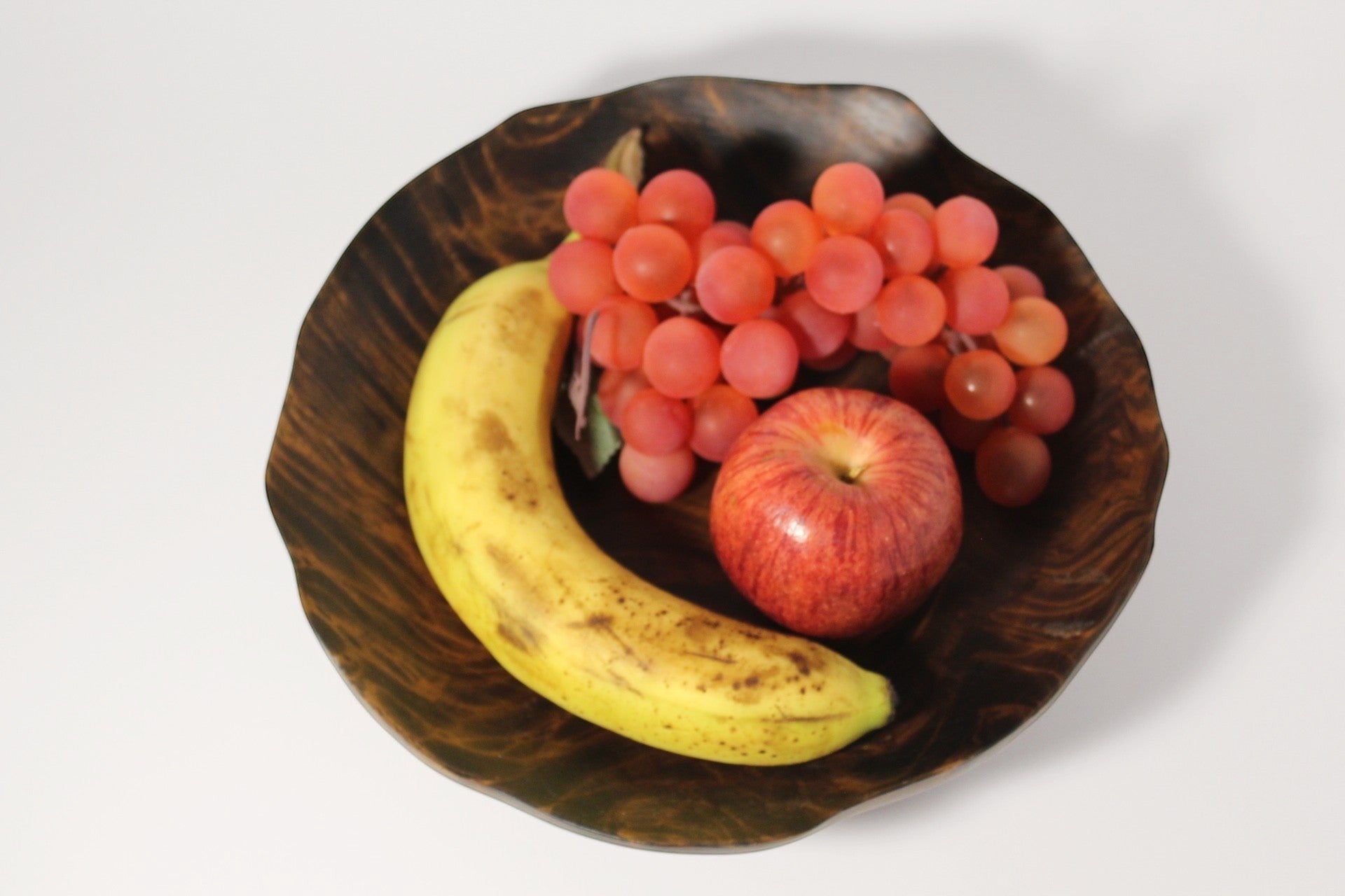 Natural Wonders USA hand carved dark wood bowl with organic shape, filled with a banana, apple, and grapes.