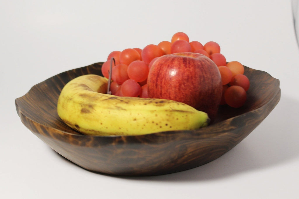 Natural Wonders USA hand carved dark wood serving bowl with organic shape and rustic rim, filled with fruit.