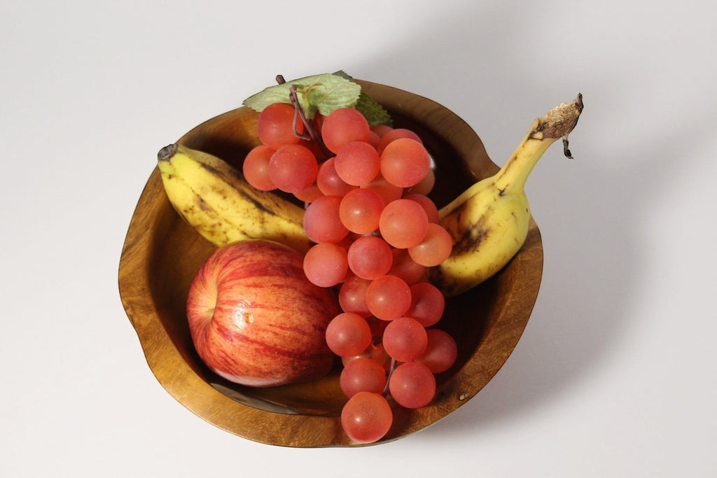 Natural Wonders USA hand carved wooden serving bowl with handles, filled with red grapes, an apple, and bananas.