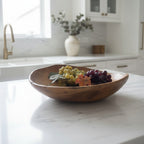 Natural Wonders USA 16" hand-crafted smooth teak serving bowl with natural wood grain, holding decorative grapes.