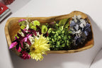 Natural Wonders USA rustic wooden trough bowl centerpiece filled with yellow, purple, and blue flowers and greenery.