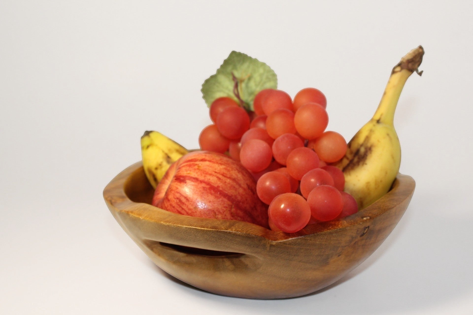 Natural Wonders USA hand carved wooden serving bowl with handles, filled with fruit. Warm wood tone.